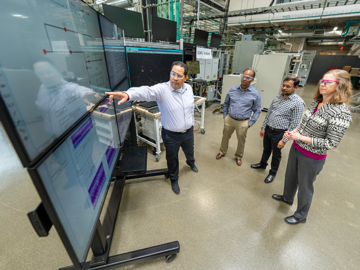 esri-78776 Four people stand around a series of flat-screen monitors as one points at an object on one of them.